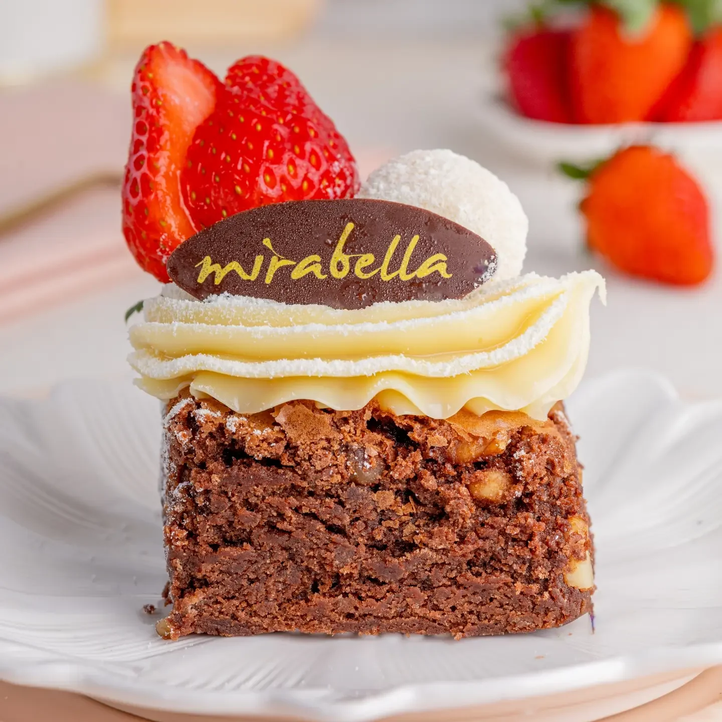 Fatia de brownie da Doceria Mirabella com creme branco, morangos e placa da marca